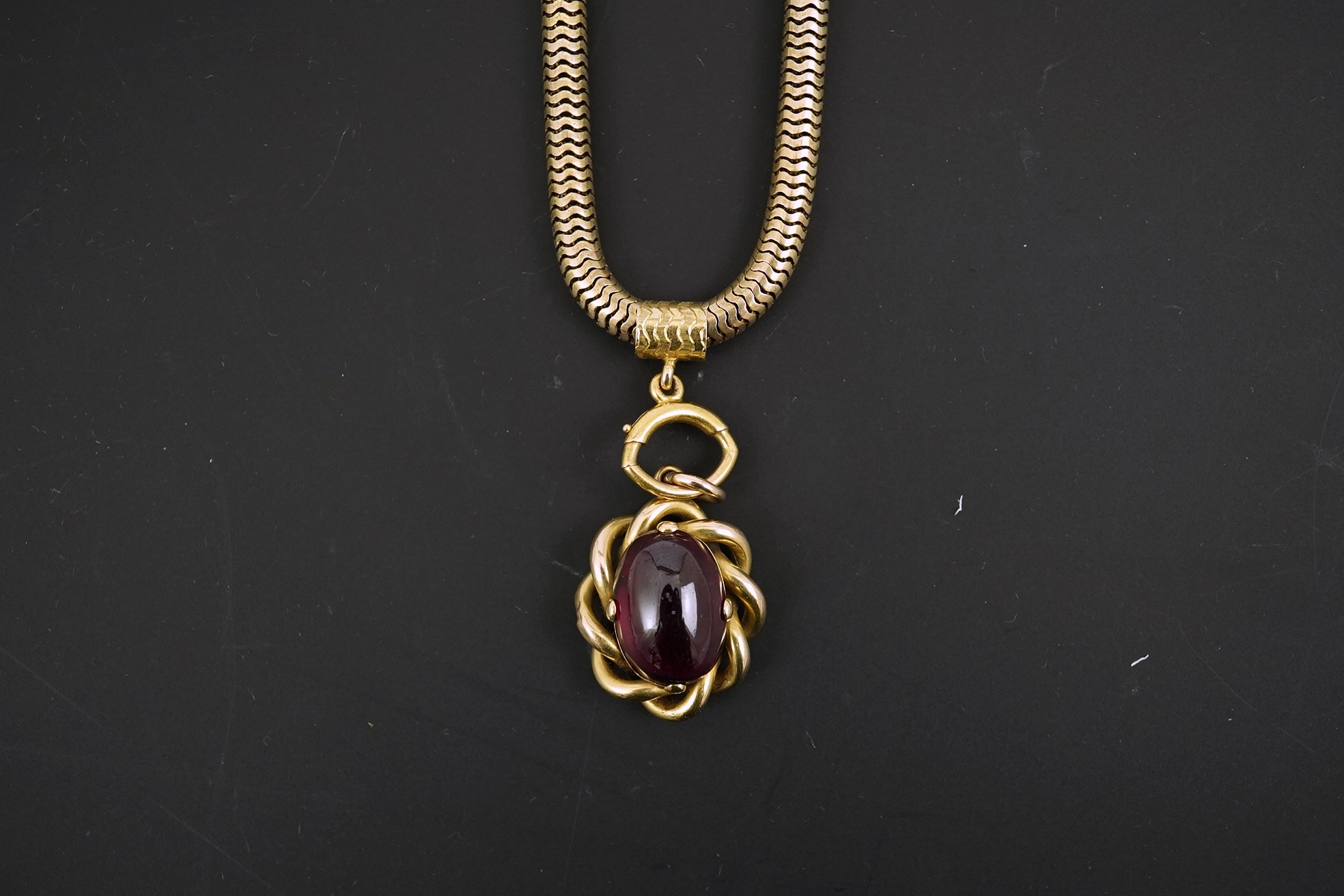 A Victorian gold snake link chain, hung with a gold and single stone oval cabochon garnet set mourning pendant